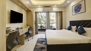 Habitación de hotel con cama, escritorio, silla, televisión y balcón con vistas.