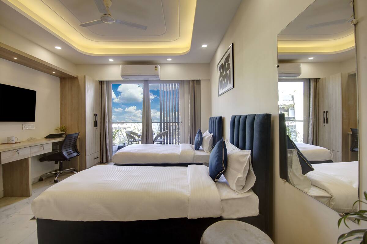 Ein modernes Hotelzimmer mit zwei Betten, einem Schreibtisch, einem Flachbildfernseher und einem Balkon mit Blick zum Himmel.