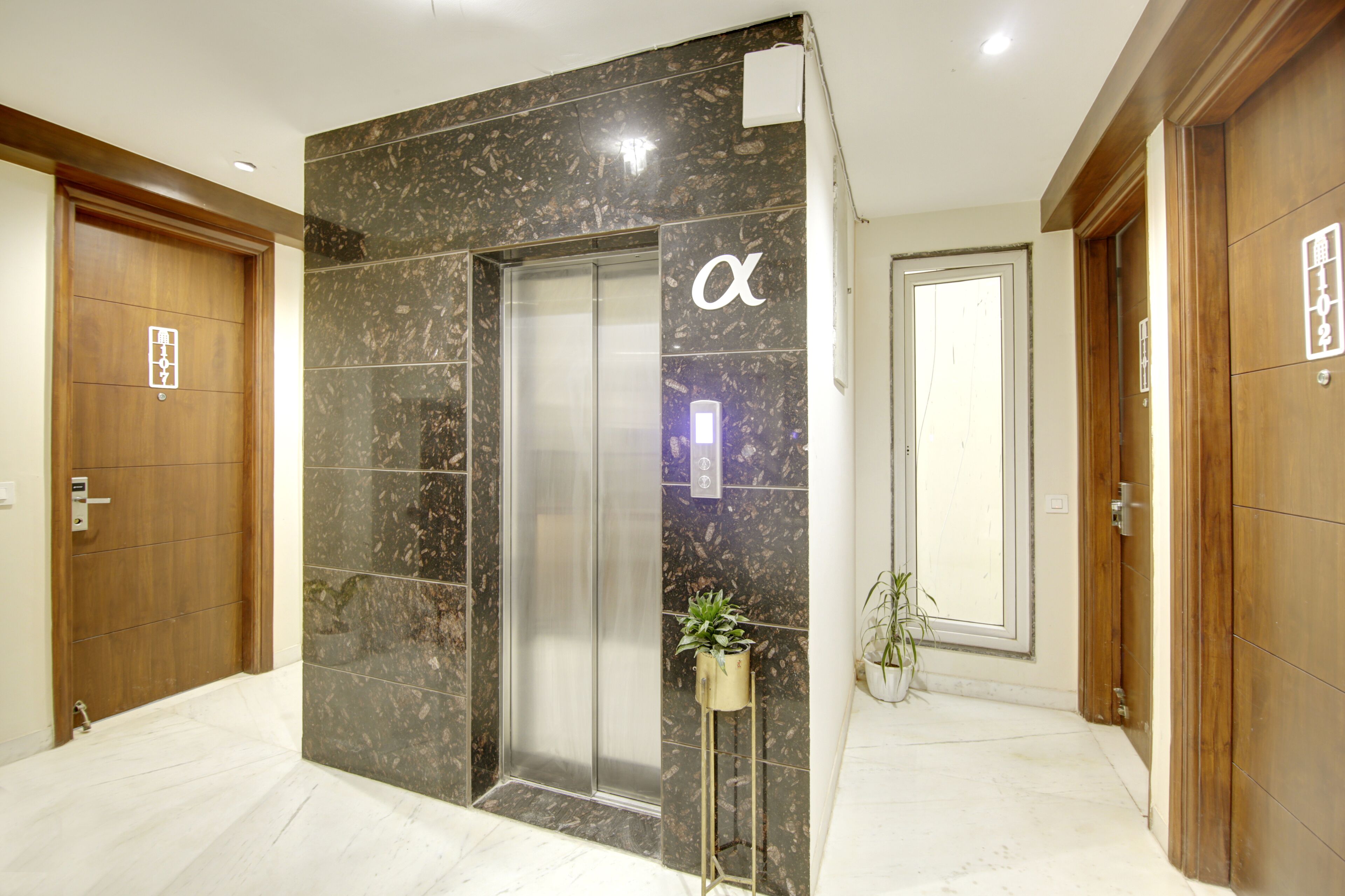 A modern elevator with a marble wall, a potted plant, and a wooden door with a sign.