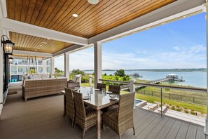 A covered outdoor area with a dining table, wicker chairs, and a sofa. It features a view of a body of water and a dock.