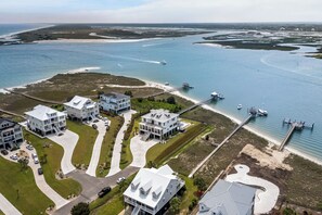 An aerial view of a coastal residential area with multiple houses, a pier, and a marina with boats.