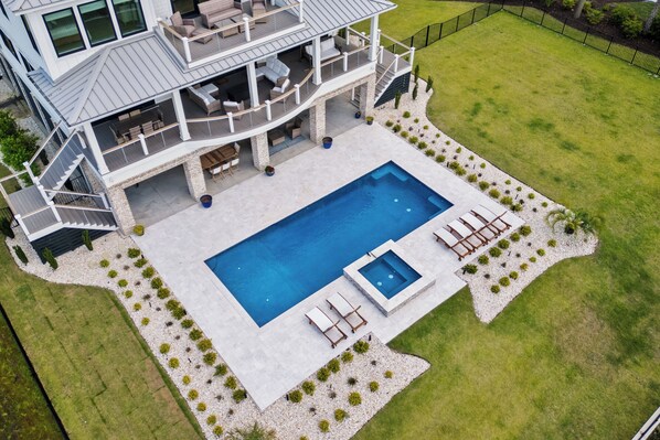 A two-story house with a large rectangular swimming pool, outdoor seating, and a well-maintained lawn.