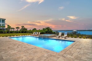 A rectangular swimming pool with a stone accent wall, surrounded by a paved patio with lounge chairs.