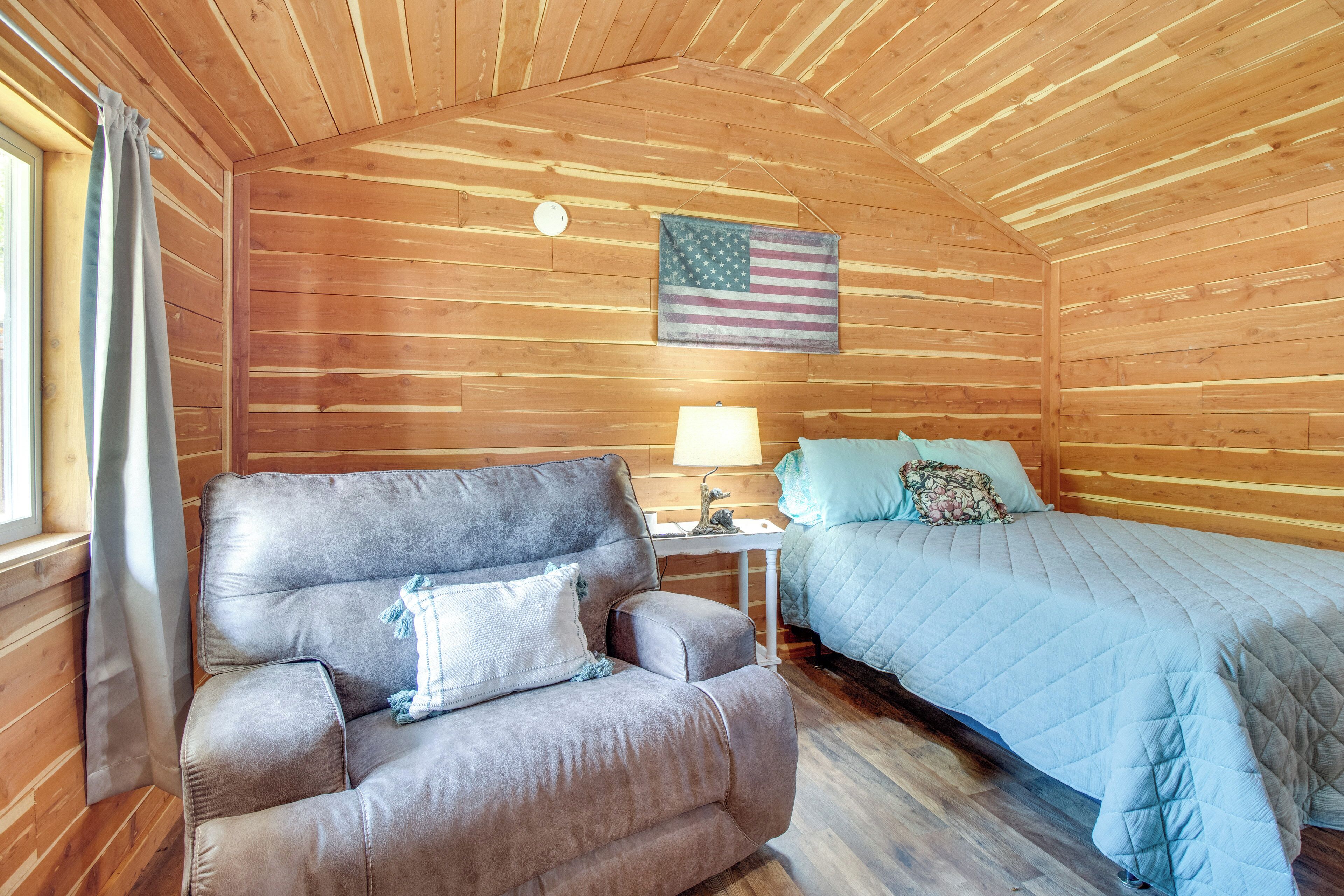 A cozy cabin room with a wooden ceiling, a couch, a bed, a nightstand, and an American flag.