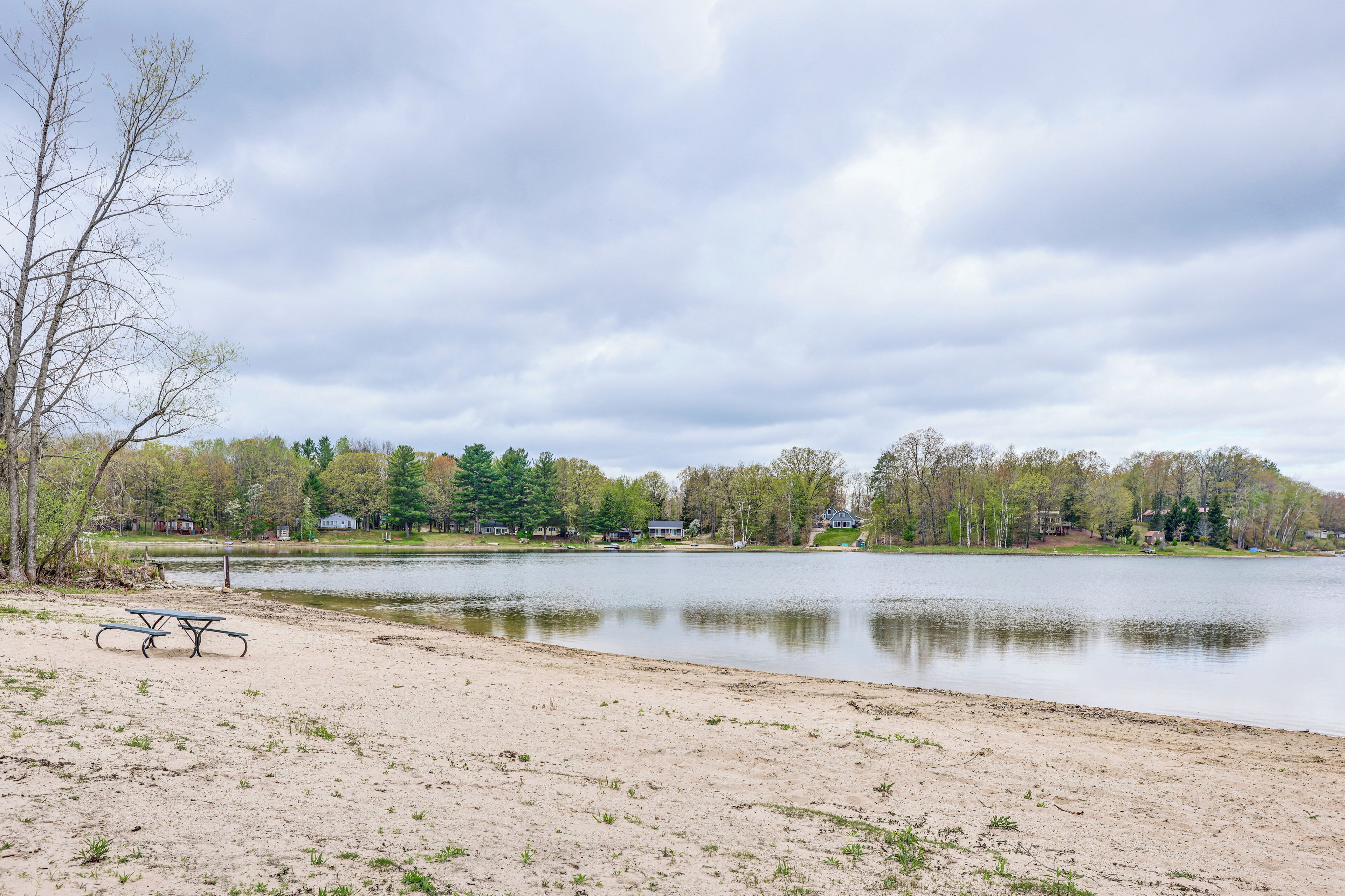 A lakeside park with a picnic table and benches, surrounded by trees and houses in the background.