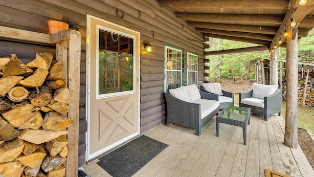 A log cabin with a porch, wicker furniture, and a firewood stack. - 2 Mi to Lake Willoughby: Peaceful Log Cabin! (West Burke)