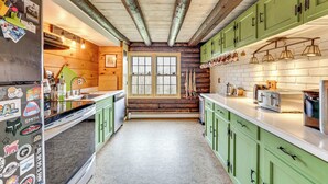 A kitchen with green cabinets, a stainless steel refrigerator, and a window with a view. - 2 Mi to Lake Willoughby: Peaceful Log Cabin! (West Burke)