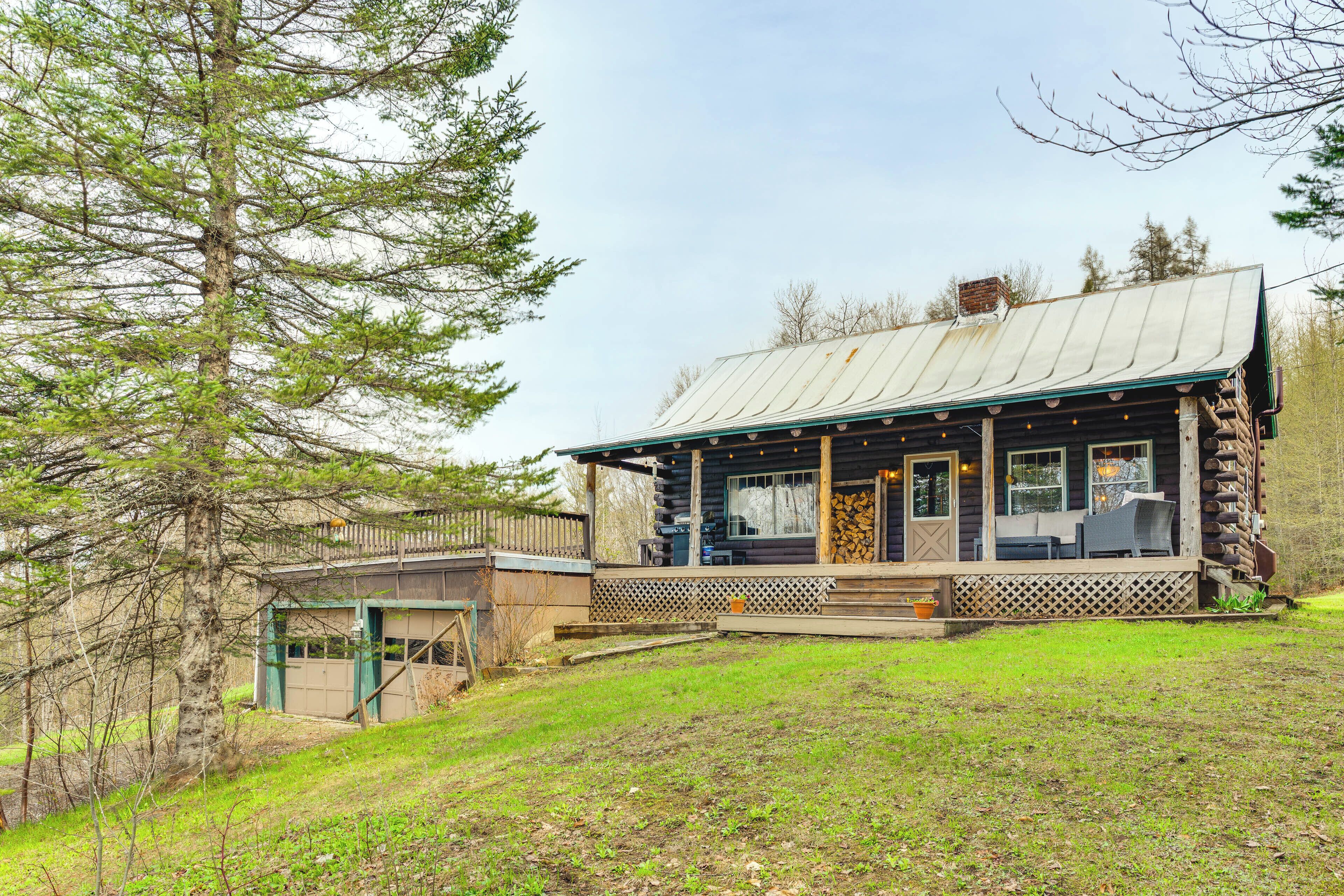 A log cabin with a porch, a covered outdoor seating area, and a view of the surrounding forest.