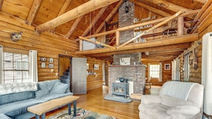 A log cabin interior with a fireplace, wooden ceiling beams, and a cozy seating area. - 2 Mi to Lake Willoughby: Peaceful Log Cabin! (West Burke)