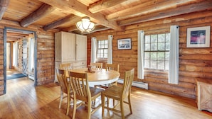 A wooden cabin interior with a round dining table, wooden chairs, and a chandelier. - 2 Mi to Lake Willoughby: Peaceful Log Cabin! (West Burke)