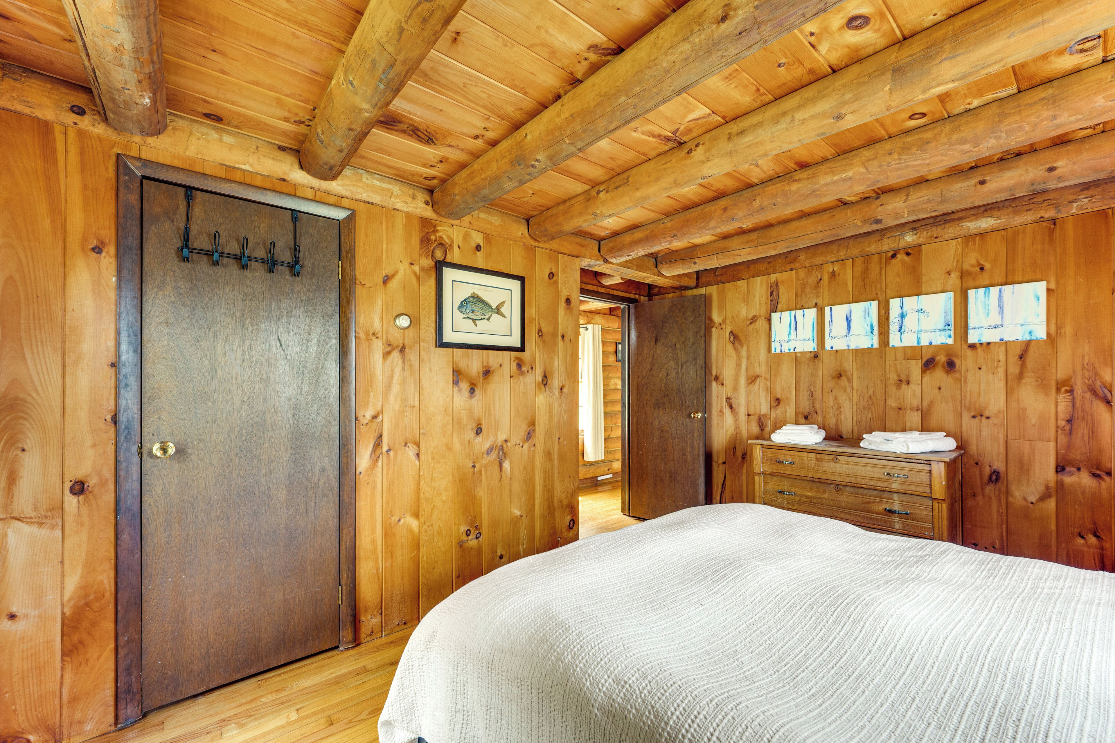 A wooden cabin bedroom with a bed, a dresser, and a door with hooks.