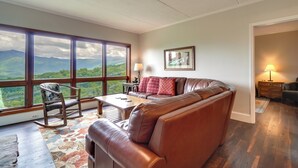 A spacious living room with a large window offering a mountain view, a leather sofa, a rocking chair, and a wooden coffee table. - 3 Mi to Gsmnp! Family Condo w/ Pool & Views (Gatlinburg)
