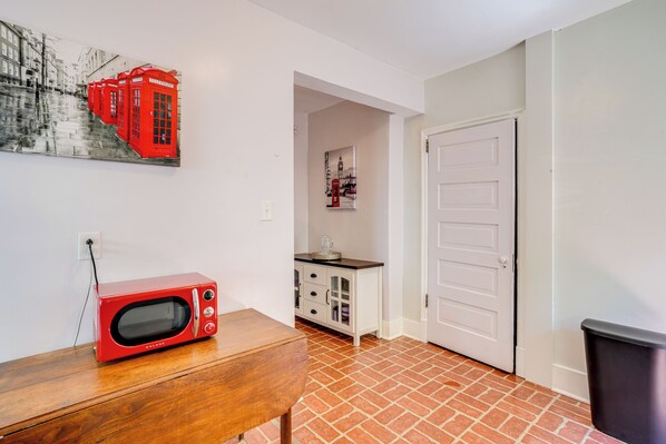 Un couloir avec un four à micro-ondes rouge posé sur une table en bois, une porte blanche et un meuble avec des tiroirs.