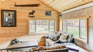 A cabin interior with a wooden ceiling, a sofa with patterned cushions, a table, and a window offering a view of the outdoors. - Fishing & Views: 'river Paradise' in Dubois! (Dubois)