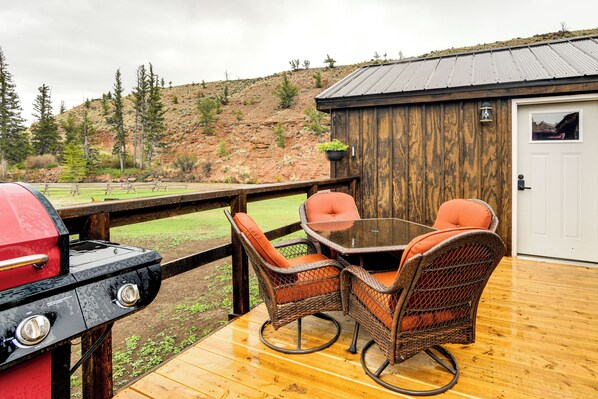 An outdoor patio with a wooden deck, wicker chairs, a glass table, and a barbecue grill. - Fishing & Views: 'river Paradise' in Dubois! (Dubois)