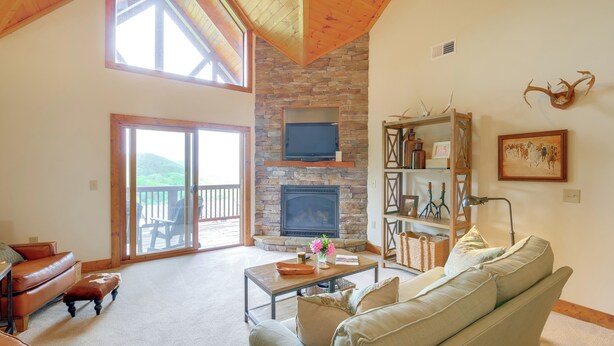 A spacious living room with a stone fireplace, leather sofas, and a large window overlooking a deck. - Mountain Condo 2 Mi to Dtwn Banner Elk w/ Views! (Banner Elk)