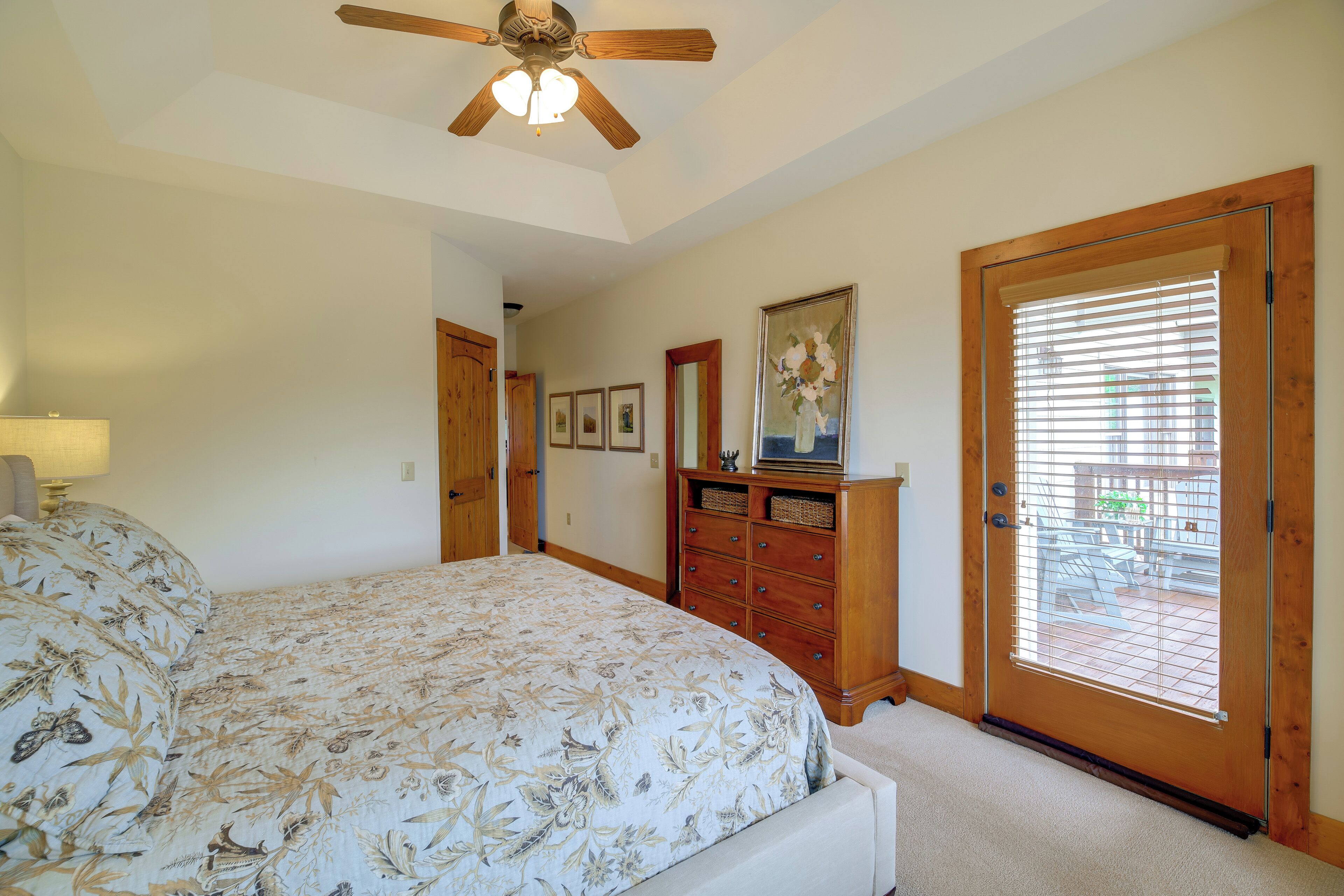 A bedroom with a large bed, wooden dresser, ceiling fan, and a door leading to a balcony.