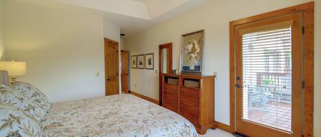 A bedroom with a large bed, wooden dresser, ceiling fan, and a door leading to a balcony.