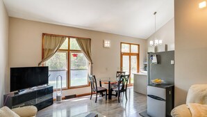 Een ruime woonkamer met een flatscreen-tv, een eettafel met stoelen, een koelkast en een bank.