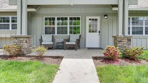 A covered porch with two chairs and a table, a stone pillar, and a door with a window.