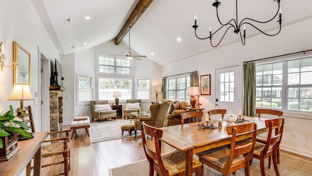 A spacious living room with a wooden dining table, comfortable seating, and large windows providing natural light.