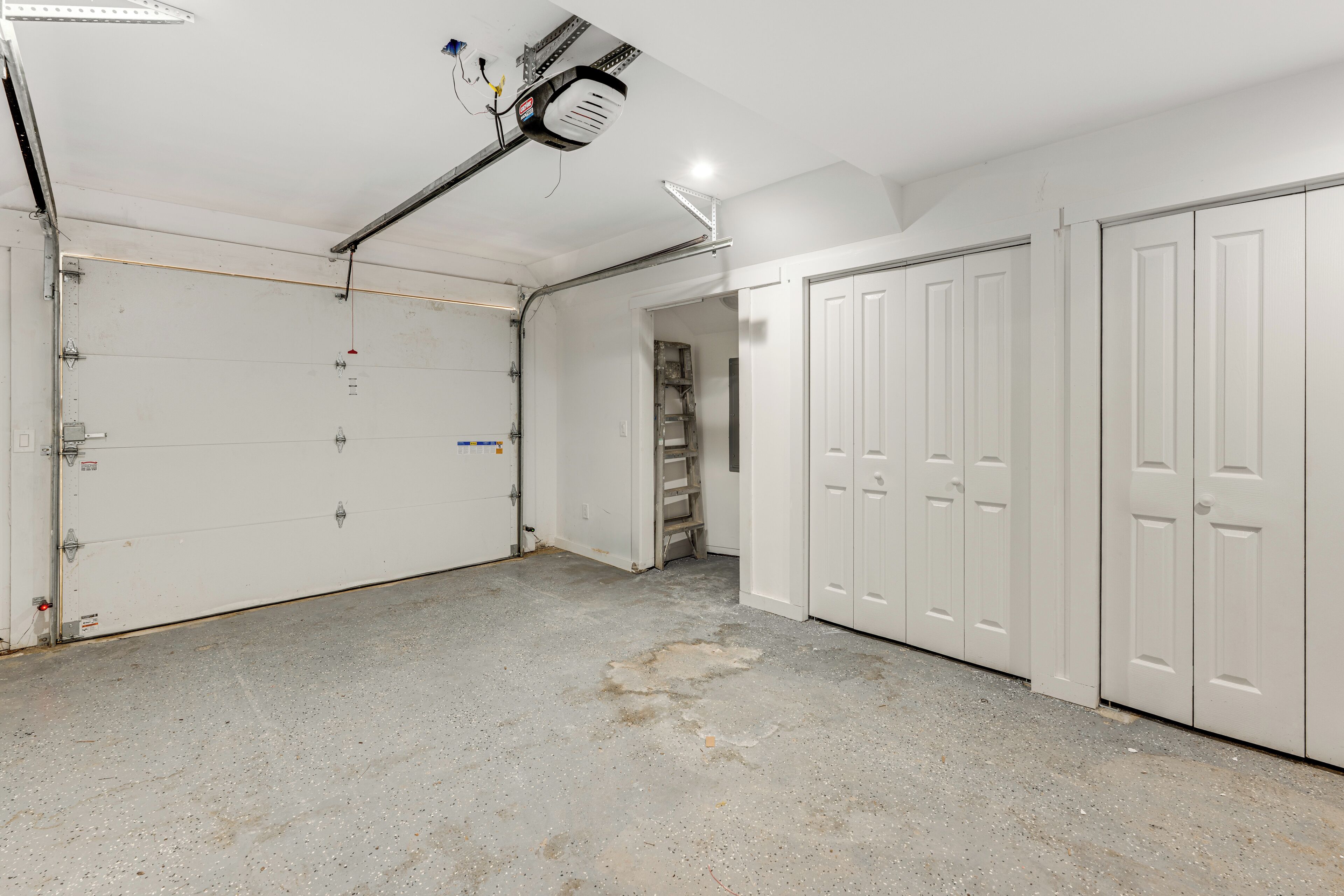 A garage with concrete floor, white garage doors, and a ceiling fan.