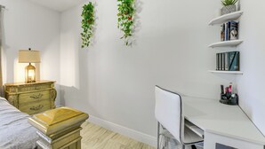 Une chambre à coucher comprenant un lit, une table de chevet, une lampe, une commode, un bureau, une chaise et des étagères avec des livres et des objets décoratifs.