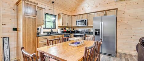 Cocina de estilo rústico con muebles de madera, una mesa y sillas, electrodomésticos de acero inoxidable y un cartel de bienvenida.