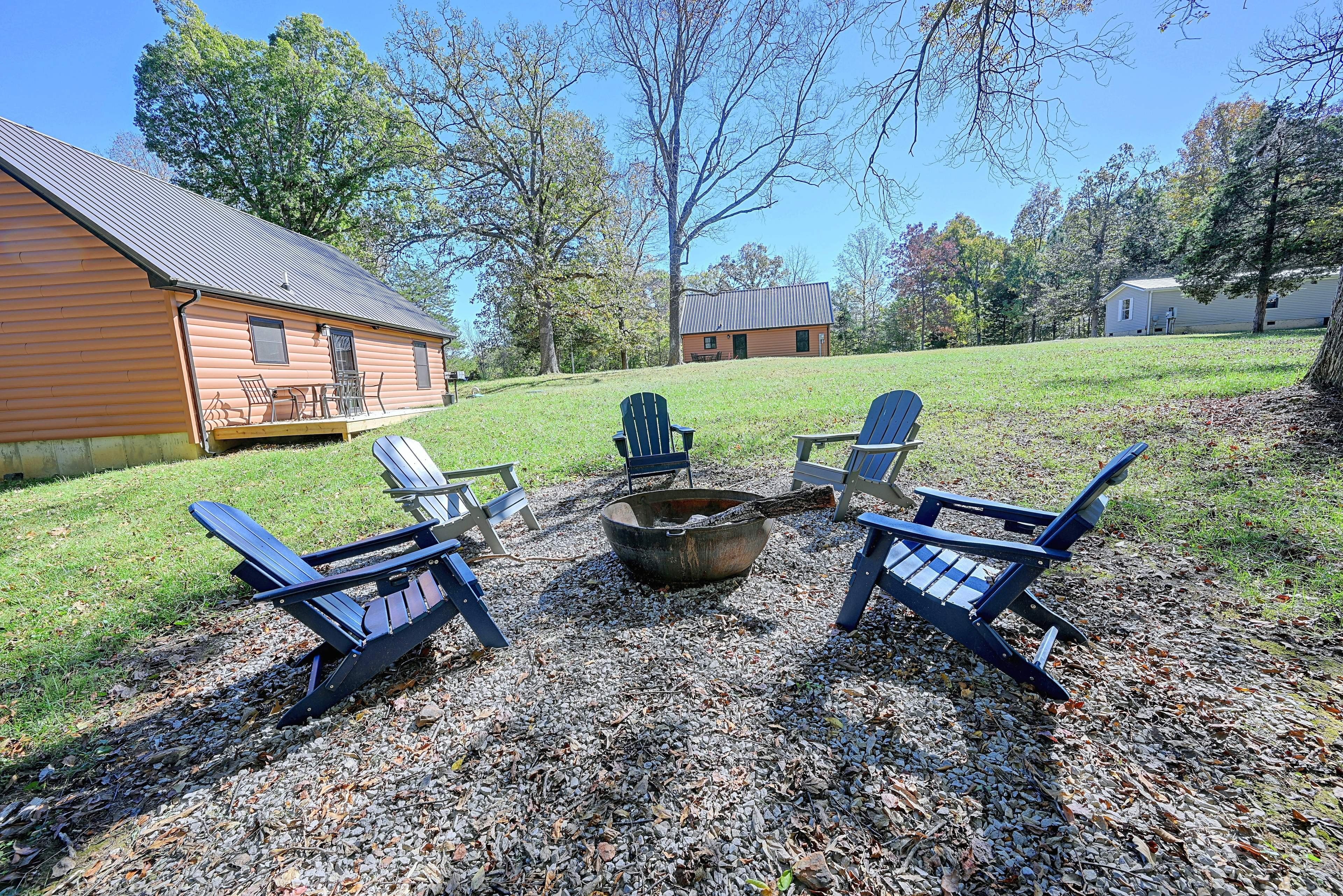 A log cabin with a deck, surrounded by a grassy area with Adirondack chairs and a fire pit.