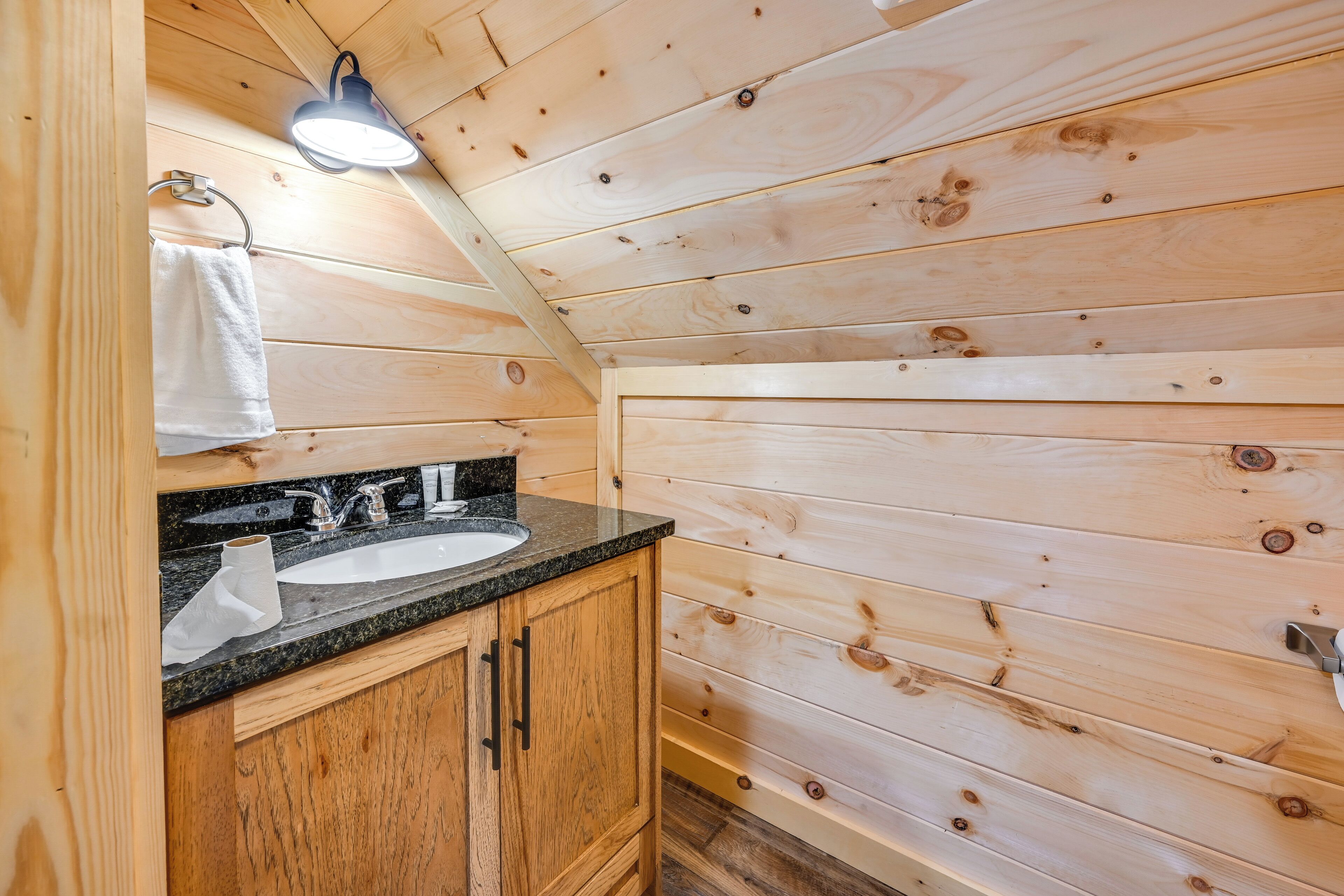 Bagno di una baita in legno, con lavandino, specchio e asciugamano appeso al muro.