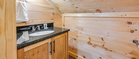 Bagno di una baita in legno, con lavandino, specchio e asciugamano appeso al muro.