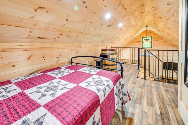 Un dormitorio abuhardillado con paneles de madera, una cama, un barril de madera y una escalera.