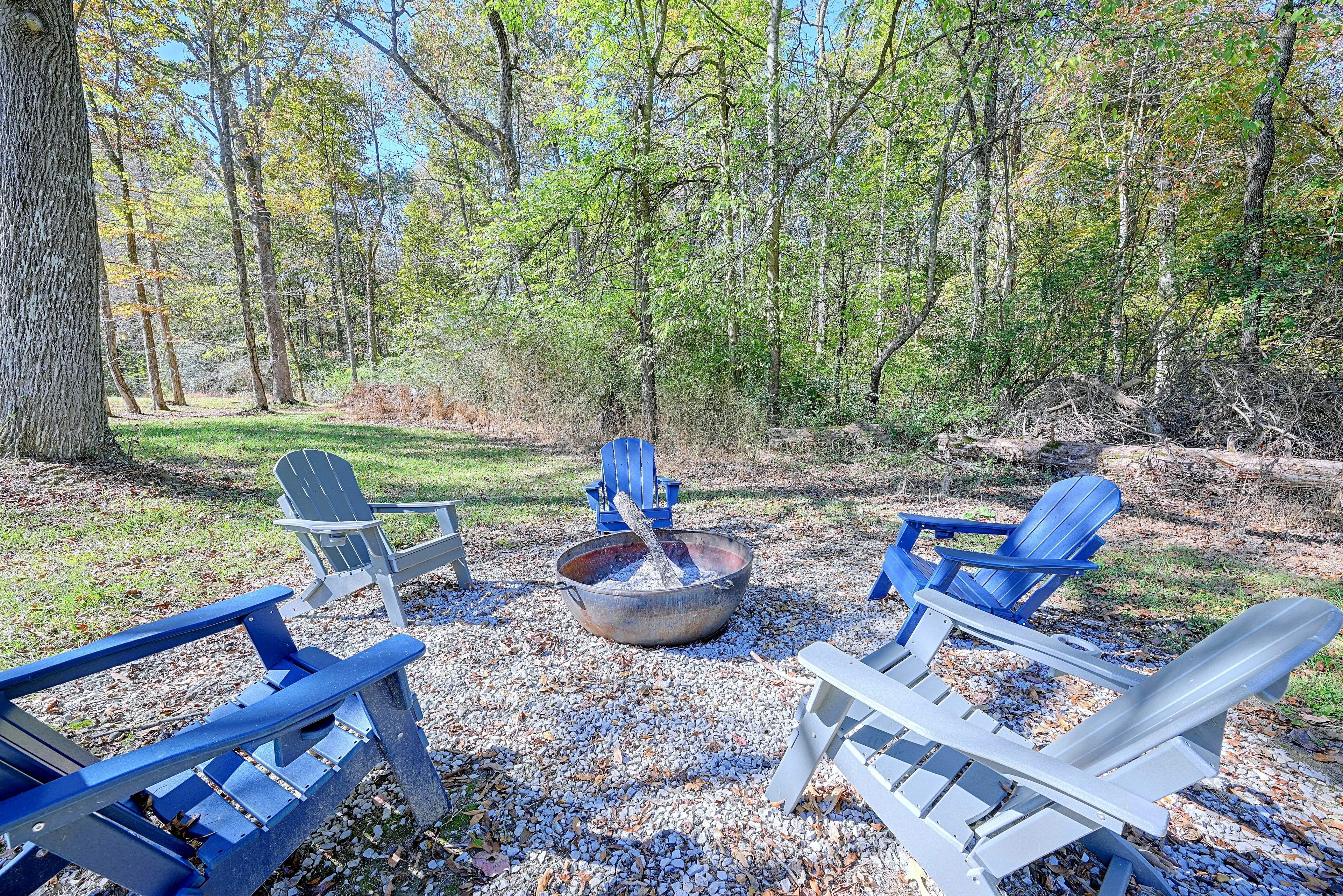 A campsite with Adirondack chairs, a fire pit, and a natural forest setting.