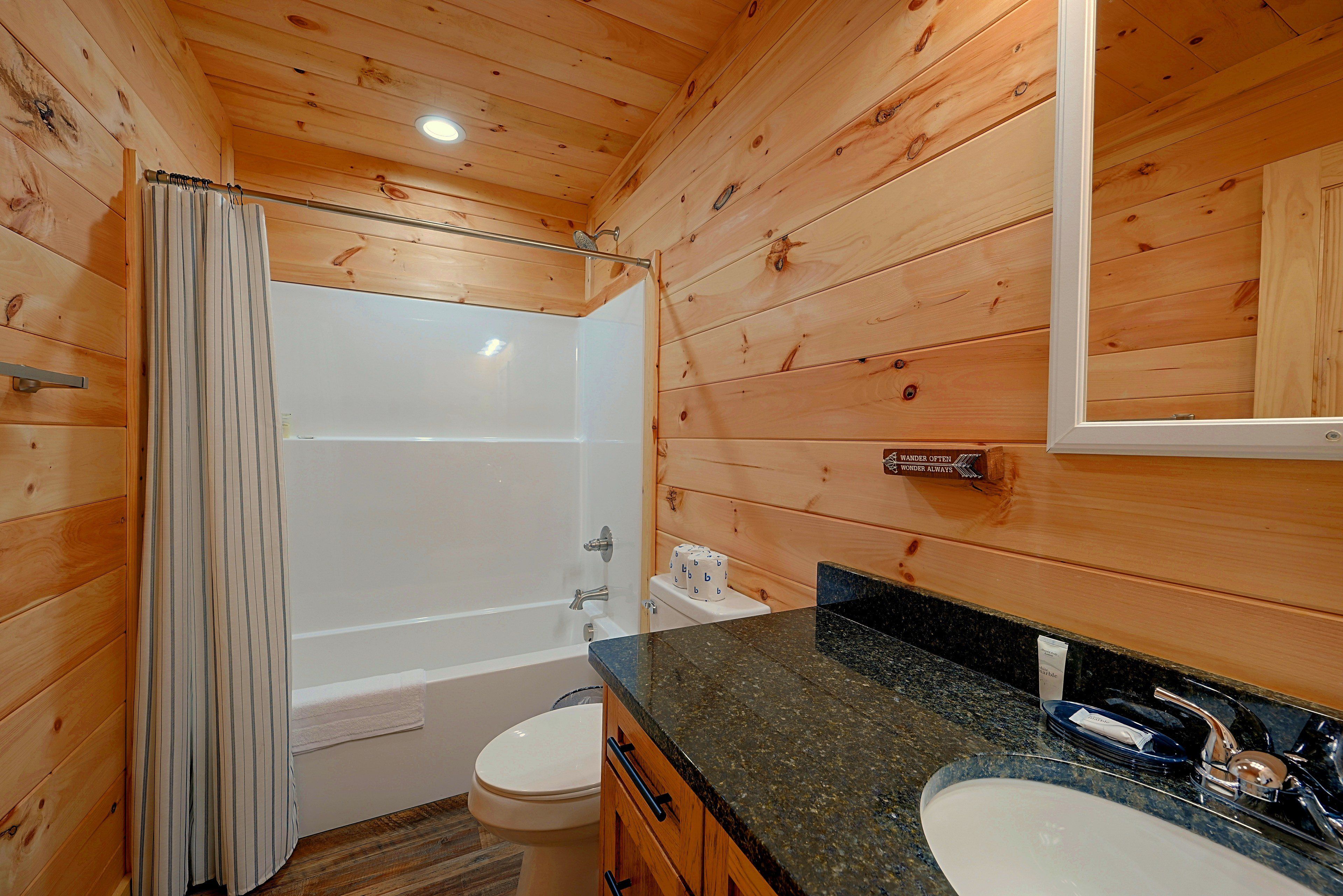 A wooden cabin bathroom with a bathtub, toilet, and vanity.