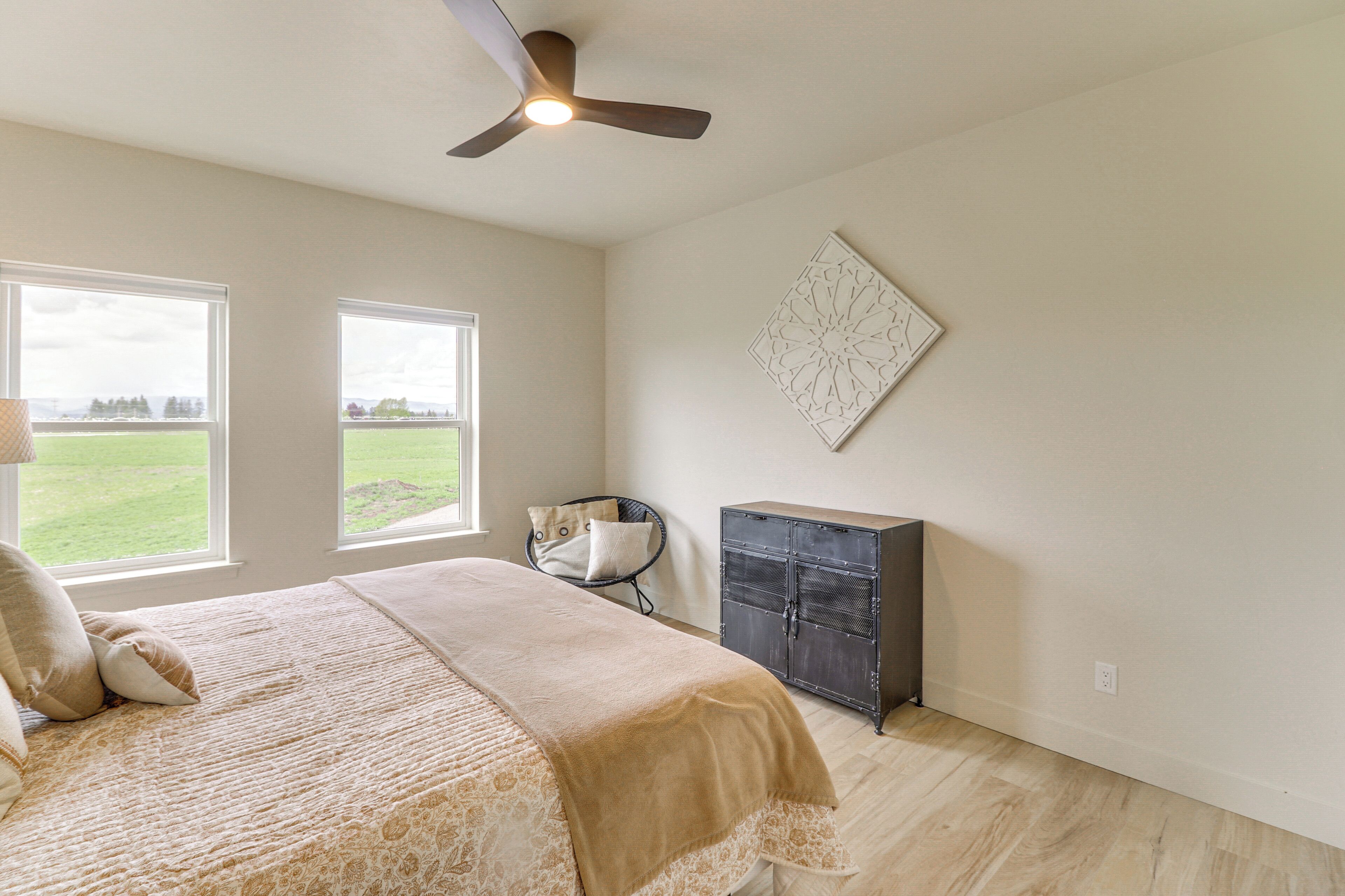 A bedroom with a bed, two windows, a ceiling fan, a cabinet, and a wall-mounted artwork.