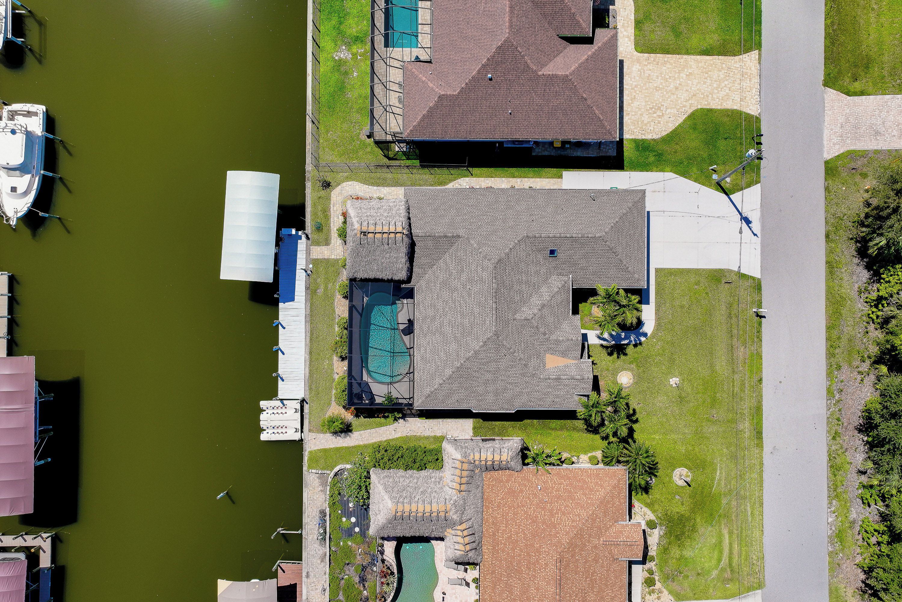 Vista aérea de uma área residencial com piscina, um píer de barcos e uma casa com telhado de palha.