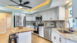 Una cocina moderna con armarios blancos, electrodomésticos de acero inoxidable, una isla de madera y un ventilador de techo.