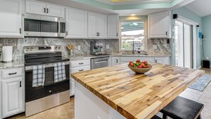 Una cocina moderna con armarios blancos, una isla grande de madera, un horno empotrado y un microondas.