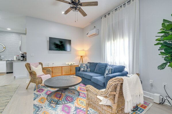A modern living room with a blue sofa, wicker chairs, a round coffee table, and a colorful rug.