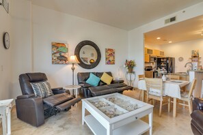 A living room with a reclining chair, a coffee table, a dining table with chairs, and a kitchen in the background. - Walk to Galveston Beach: Family Condo w/ Pool (Galveston)