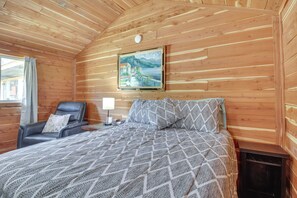 Una habitación acogedora de madera con una cama, una silla y un cuadro en la pared.