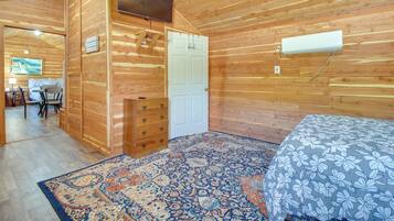 A wooden-paneled room with a bed, a dresser, a door, and a mounted air conditioner.
