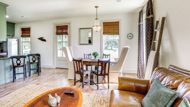 A spacious living area with a dining table, leather sofa, and a kitchen in the background. - 2 Mi to L'auberge Casino: Home w/ Large Yard! (Baton Rouge)