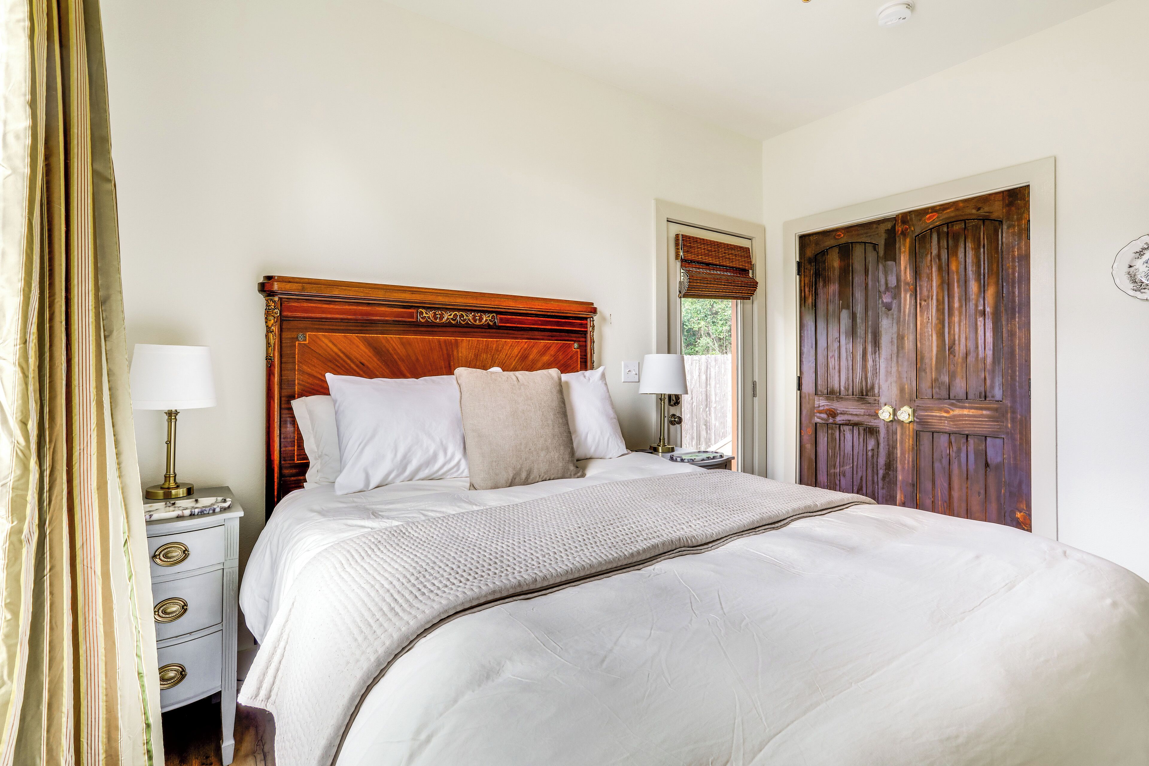 A neatly made bed with a wooden headboard, two bedside tables with lamps, and a large wooden door.