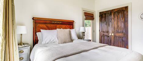 A neatly made bed with a wooden headboard, two bedside tables with lamps, and a large wooden door.