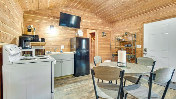 L’intérieur d’un chalet en bois comprend une cuisine, un coin repas et un téléviseur fixé au mur.