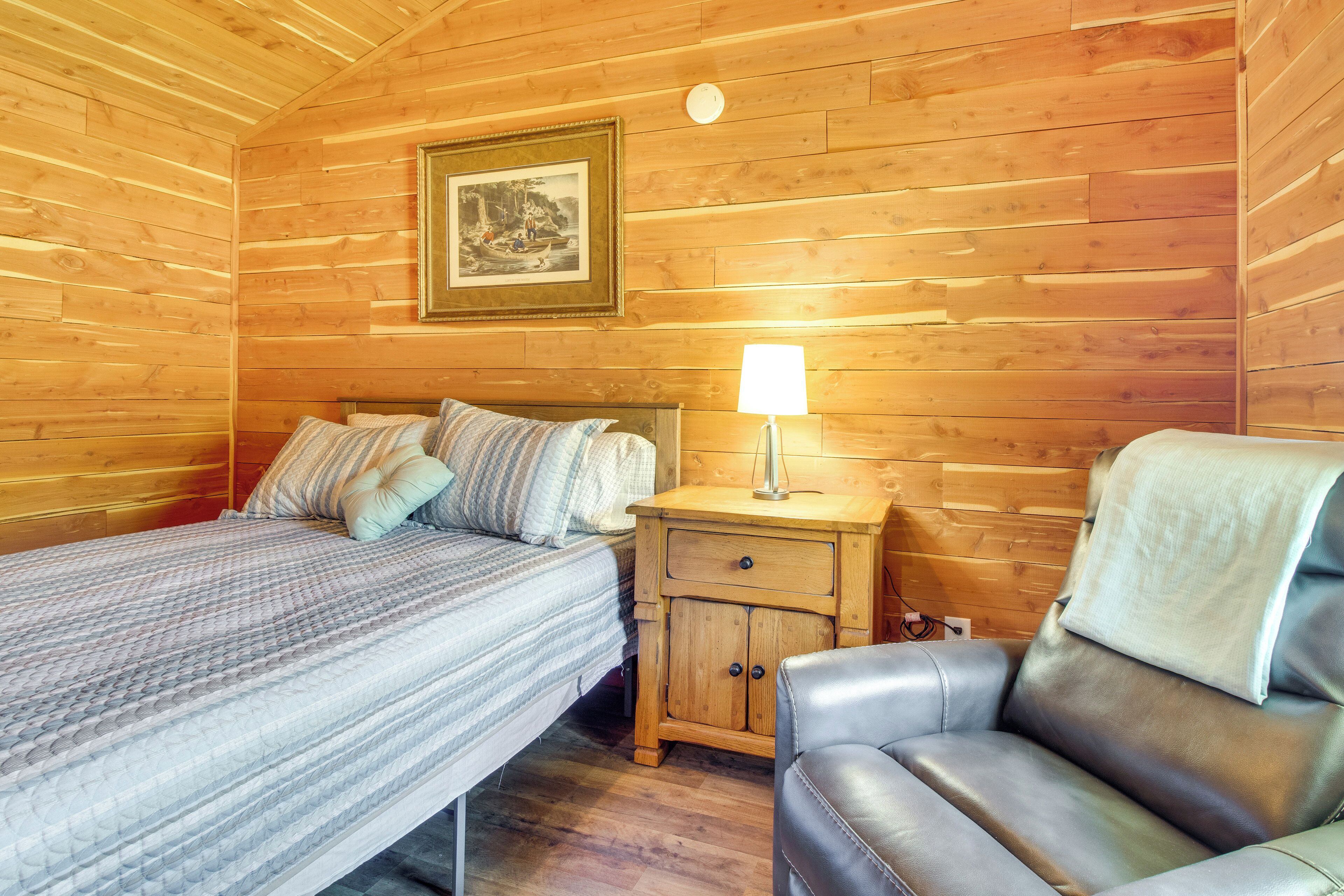 Una habitación con paneles de madera, una cama, una mesita de noche con lámpara y un sillón de cuero.