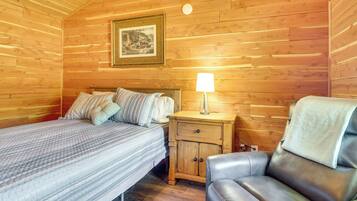 Una habitación con paneles de madera, una cama, una mesita de noche con lámpara y un sillón de cuero.