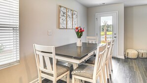 A dining area with a dark wooden table and white chairs, a vase with red flowers, and a door leading outside. - 3 Mi to Shore: Family Townhome in Surfside Beach (Surfside Beach)