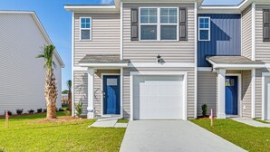 A two-story residential building with a front garage, a blue door, and a well-maintained lawn. - 3 Mi to Shore: Family Townhome in Surfside Beach (Surfside Beach)